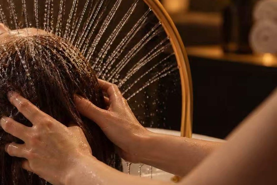 A therapist’s hands working through wet hair under the warm-water fan at Flora Spa